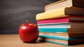 Classic school still life with a red apple next to a stack of colorful textbooks, against a dark chalkboard. Royalty Free Stock Photo