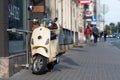 A classic, elegant Vespa scooter parked on a pedestrian sidewalk in the city center street