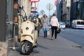 A classic, elegant Vespa scooter parked on a pedestrian sidewalk in the city center street