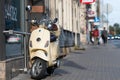 A classic, elegant Vespa scooter parked on a pedestrian sidewalk in the city center street