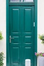 Classic European deep green door, with glass panel and brass handle, flanked by potted pink flowers and greenery Royalty Free Stock Photo