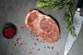 Classic fresh ribeye steak with red pepper and sprigs of rosemary on a metal plate next to a kitchen knife