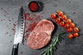 Classic fresh ribeye steak with red pepper sprinkles in a black saucer, rosemary sprigs and cocktail tomatoes on a metal plate