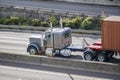 Classic gray bonnet American big rig semi truck transporting container on flat bed semi trailer moving fast on the multilevel