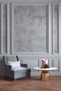 Classic gray interior with gray armchair, coffee table, flowers and wall moldings.