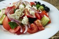 Classic Greek salad with tomatoes, onions, cucumber, feta cheese and black olives in white plate on a light background. Close up Royalty Free Stock Photo