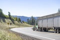 Classic green day cab big rig semi truck transporting cargo in bulk semi trailer moving on the winding mountain narrow road Royalty Free Stock Photo