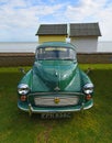 Classic Green Morris Minor with AA Badge parked with beach huts and ocean in background. Royalty Free Stock Photo