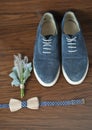 Classic groom accessories: wooden bow tie and blue shoes on a wooden table.