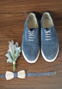 Classic groom accessories: wooden bow tie and blue shoes on a wooden table.