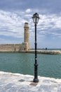 A classic lantern in the foreground and on the other side of the old harbor The ancient Rethymnon Lighthouse in Rethimno, Crete, G Royalty Free Stock Photo