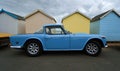 Classic Light Blue Triumph TR5 2500 PI Motor Car parked on seafront promenade with beach Huts in background.