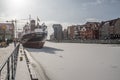 Old cargo trade ship or a steamer mooring in ice during winter in Old Town of Gdansk Poland. Old town in the background.