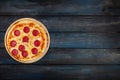 Classic pepperoni pizzai on a wooden stand on a dark wooden background. Top view orientation on the left side