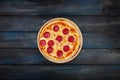 Classic pepperoni pizzai on a wooden stand on a dark wooden background. Top view center orientation