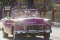Classic pink vintage car with passengers cruising down the street