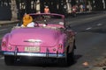 Classic pink vintage car with passengers cruising down the street