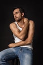 Classic portrait of young handsome bearded sad man in white undershirt and jeans isolated on dark background. Emotions Royalty Free Stock Photo