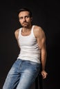 Classic portrait of young handsome bearded sad man in white undershirt and jeans isolated on dark background. Emotions Royalty Free Stock Photo