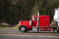 Classic powerful red big rig semi truck running on the road with