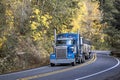 Classic powerful blue American big rig semi truck tractor transporting cargo in covered bulk semi trailer moving on the winding Royalty Free Stock Photo