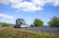Classic powerful green big rig bonnet semi truck tractor running on summer road with cloud sky Royalty Free Stock Photo