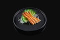 Classic raw prawn or shrimp sashimi with cucumber and daikon radish on a stylish black ceramic plate on a black background.