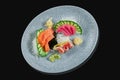 Classic raw set of sashimi salmon, seabass and tuna with cucumber and daicon on a stylish black ceramic plate on a black