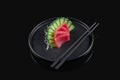 Classic raw tuna sashimi with daicon raddish on a stylish black ceramic plate on a black background. Japanese traditional food.