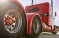 Classic red American semi truck in parking lot, detail of aluminum tandem axles with red hub caps. Low angle, rear view of big rig