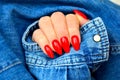 Classic red glossy nails on women hand and blue jeans jacket background