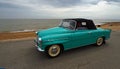 Classic Skoda Felicia Convertible being driven on seafront promenade beach and sea in the background.