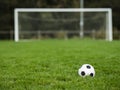 Classic soccer of football ball on the dark green grass field in focus. Goal post out of focus in the background. World wide