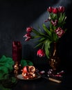 Classic still life with beautiful red tulip flowers and candle, pomegranate, green napkins that appeared in a vintage vase. Royalty Free Stock Photo