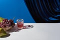 Classic still life with grape, glass with drink on white table near velour curtain isolated on blue