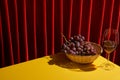 Classic still life with grape in wicker basket near glass of red wine on yellow table near red curtain Royalty Free Stock Photo