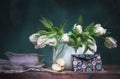 Classic still life with white tulips, half an apple and an envelope on old wooden table on green background