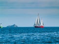 Classic style yacht with red hull sails past green buoy on beautiful deep blue sea