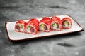 Classic sushi california roll in tobiko caviar with tuna, cucumber and cream cheese on a white plate on a gray background. Close Royalty Free Stock Photo