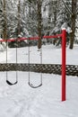 Classic swing set in a public park, red support stand and black rubber swing seats, snowy day