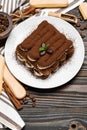 Classic tiramisu dessert on ceramic plate and savoiardi cookies on wooden background