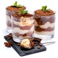 Classic tiramisu dessert in a glass cup on stone serving board and pieces of chocolate on white background with clipping
