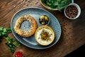 Classic Turkish breakfast - simit with feta cheese mousse with olive oil and spices, served on blue plate with olives. Wood