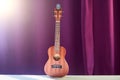 Classic ukulele on purple background. Small wooden guitar on curtains background. Ukulele stands on a white table