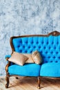 Classic vintage blue buttoned sofa with golden cushions on gray concrete wall indoors, copy space. Living room interior. Royalty Free Stock Photo