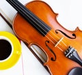 The classic violin and bow put beside half of yellow ceramic coffee cup Royalty Free Stock Photo