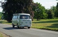 Classic Volkswagen Camper Van driving though village cottage and trees in the backgro