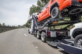 Classic white big rig car hauler semi truck transporting cars on two level semi trailer driving on the wide highway road