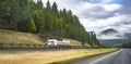 Classic white big rig semi truck transporting commercial cargo on flat bed semi trailer running on the road on the hillside with Royalty Free Stock Photo