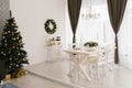 Classic white living room or dining room with a wooden white table and chairs, a Christmas tree and brown curtain Royalty Free Stock Photo